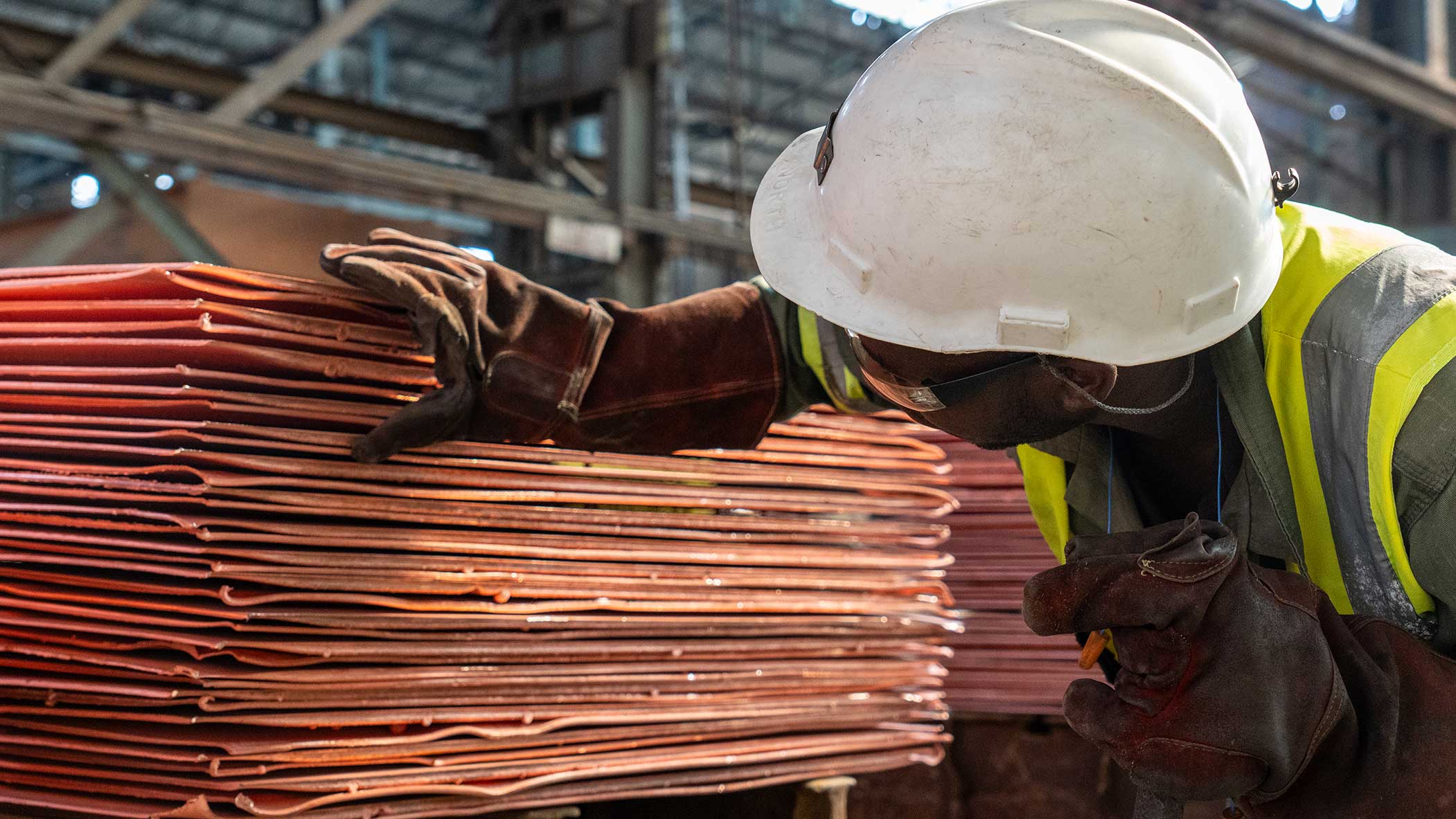 IRH worker inspecting stacked copper cathode sheets at Mopani Copper Mines